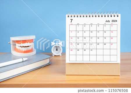 July monthly desk calendar for 2024 year and model dentures on the table. 115076508