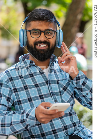 Happy Indian man dancing in wireless headphones listening favorite energetic music on city street Happy Indian man dancing in wireless headphones listening favorite energetic music on city street 115076722