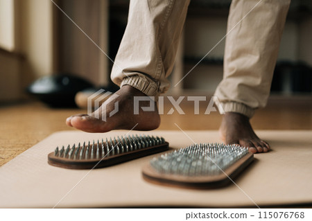 Closeup of unrecognizable black male feet stepping on sadhu board enjoying mindful practice in sunny meditation room. Concept of alternative medicine, recreational activities, mindfulness, tranquility 115076768
