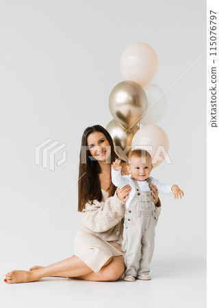 Happy woman and child pose for a photo with golden and white balloons. The scene is happy and joyful Happy woman and child pose for a photo with golden and white balloons. The scene is happy and joyful 115076797