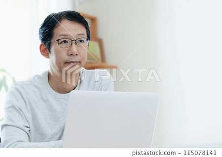 A middle-aged man thinking while looking at a computer A middle-aged man thinking while looking at a computer 115078141