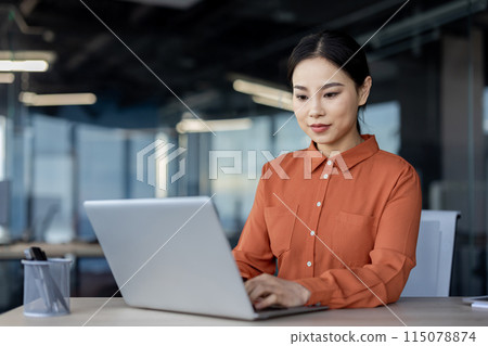 Serious thinking asian woman working inside office with laptop, business woman typing on keyboard, business woman financier preparing electronic report, report on company's financial results. 115078874