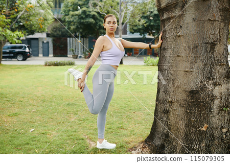 Woman Stretching Leg Against Tree in Park Woman Stretching Leg Against Tree in Park 115079305