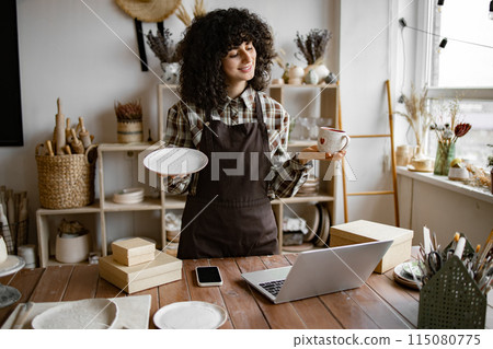 Attractive curly woman wearing brown apron receiving goods. Attractive curly woman wearing brown apron receiving goods. 115080775