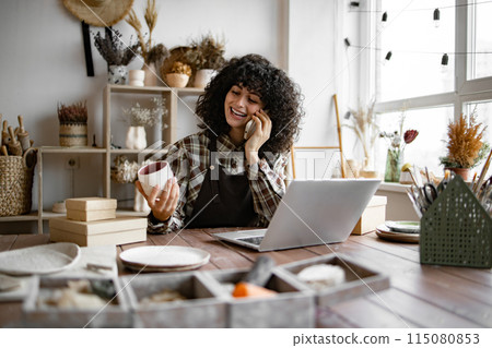 Woman potter taking order for purchase of tableware using phone and laptop. 115080853