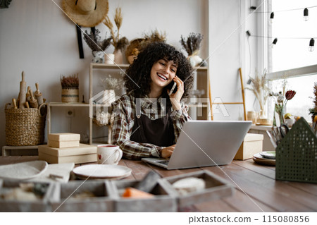 Woman potter taking order for purchase of tableware using phone and laptop. 115080856