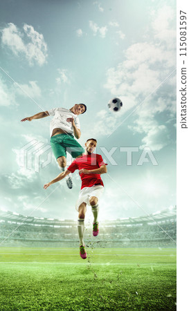 Dynamic image of two soccer players in mid-air, competing to head soccer ball on lush green soccer field, with large stadium filled of fans on background. 115081597