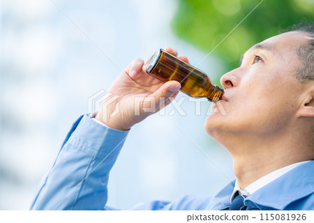Man in work clothes, outside the car, energy drink 115081926