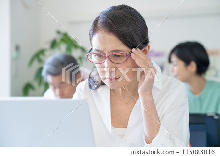 Senior woman with presbyopia having difficulty seeing a computer screen 115083016