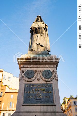 This image shows the Monument to Giordano Bruno, a philosopher and Dominican friar, in Campo de Fiori, Rome, Italy. The monument features a statue of Bruno, standing tall and proud on a pedestal. 115083810