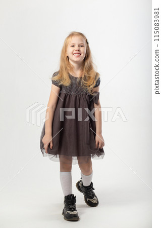A little blonde girl in a dress and black boots poses 115083981