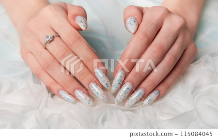 Elegant Hands Featuring Sparkling Ring and Blue Floral Manicure on Delicate White Fabric 115084045