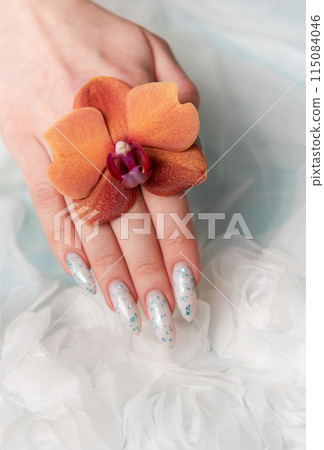 Showcasing Floral Nail Art and Holding an Orange Blossom on a Soft Textured Surface 115084046