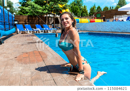 Happy young woman in swimsuit posing in hotel pool. Attractive slim lady with smooth skin smiling in water pool 115084621