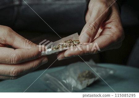 man about to roll a joint, sitting at a table man about to roll a joint, sitting at a table 115085295