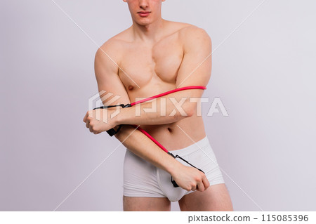 Athlete with a muscular body in white panties is doing physical exercises with rubber 115085396