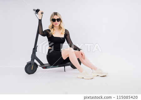 Beautiful emotional young female in sport clothes on electric scooter on red and white background 115085420