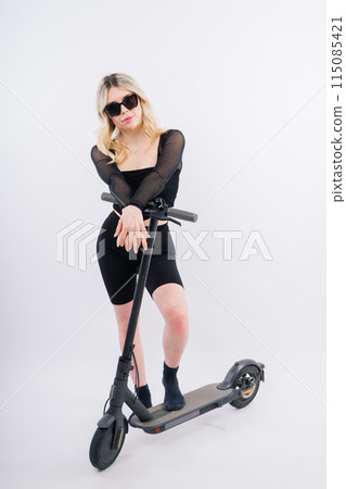 Beautiful emotional young female in sport clothes on electric scooter on red and white background Beautiful emotional young female in sport clothes on electric scooter on red and white background 115085421