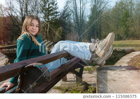 Beautiful teen girl on a bench in the park. Single girl on a bench. Beautiful teen girl on a bench in the park. Single girl on a bench. 115086375