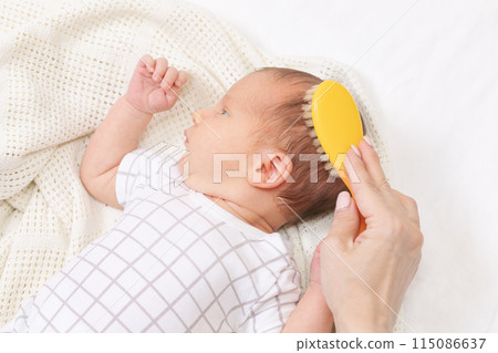 Mother gently brushing her newborn babys hair 115086637