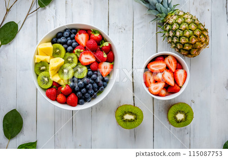 Fresh Fruit Salad with Strawberries, Blueberries, Kiwis, and Pineapple on White Wooden Table 115087753