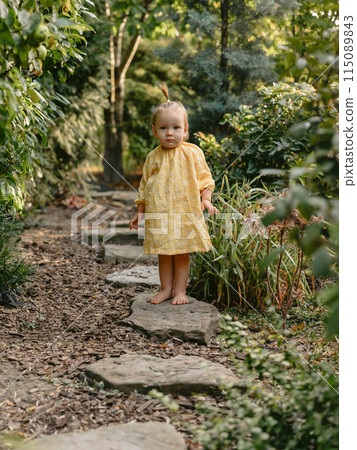 Cute child girl eat apple fruit. Little girl close up in summer garden. 115089843