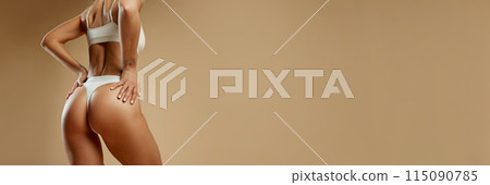 Banner. Woman with fit and toned lower body poses in white lingerie, showcasing her sculpted buttock against beige studio background. Banner. Woman with fit and toned lower body poses in white lingerie, showcasing her sculpted buttock against beige studio background. 115090785