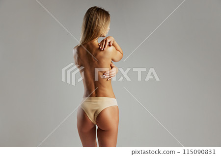 Fit woman from behind, highlighting her defined back and beige ribbed lingerie against grey studio background. 115090831
