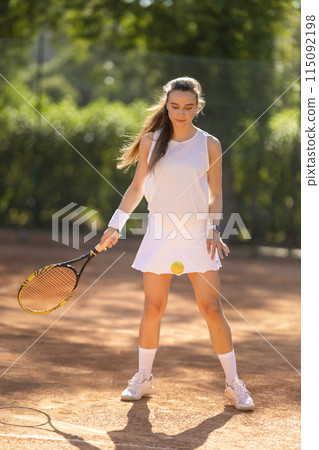 A woman in a white tennis outfit is holding a tennis racket 115092198