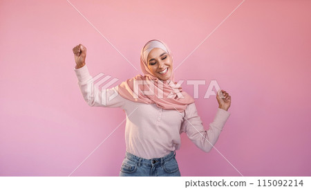 Winner dance. Victory joy. Happy delighted carefree woman in hijab enjoying freedom energy isolated on pink copy space background. 115092214