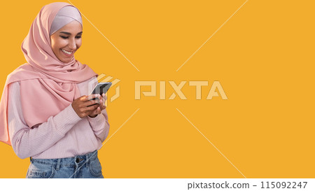 Mobile chat. Online communication. Social media. Happy smiling woman in hijab using phone texting message isolated on orange empty space background. Mobile chat. Online communication. Social media. Happy smiling woman in hijab using phone texting message isolated on orange empty space background. 115092247
