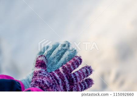 A pair of mismatched gloves on a child held over a white snow background A pair of mismatched gloves on a child held over a white snow background 115092660
