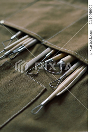 Vertical high angle closeup of set of clay carving tools in apron pocket, copy space 115096602