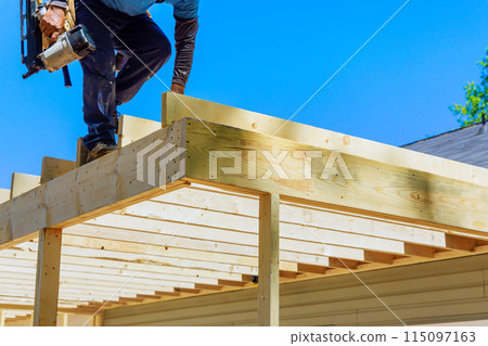 In nailing wooden plank frame together, framer worker uses an air nails hammer to install beams 115097163