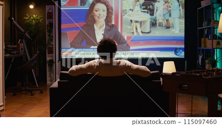 Man in home theatre watching huge TV screen showing news broadcast reportages on family trips. Zoom in shot on cord cutter looking at streaming service travelling channel on widescreen television set Man in home theatre watching huge TV screen showing news broadcast reportages on family trips. Zoom in shot on cord cutter looking at streaming service travelling channel on widescreen television set 115097460