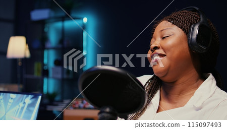 Zoom in on african american woman streaming podcast using vlogging camera during live political debate on vlog channel. Internet show presenter in dimly lit studio, close up Zoom in on african american woman streaming podcast using vlogging camera during live political debate on vlog channel. Internet show presenter in dimly lit studio, close up 115097493