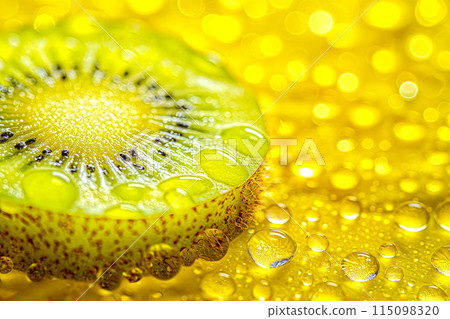 A slice of kiwi fruit is on a yellow surface with water droplets on it 115098320