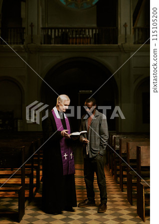 Vertical long shot of senior Caucasian priest and African American man standing at Catholic church nave discussing religious text Vertical long shot of senior Caucasian priest and African American man standing at Catholic church nave discussing religious text 115105200