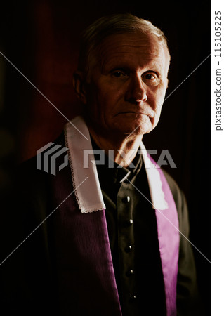 Vertical low key medium closeup portrait of elderly Caucasian Catholic priest looking at camera Vertical low key medium closeup portrait of elderly Caucasian Catholic priest looking at camera 115105225