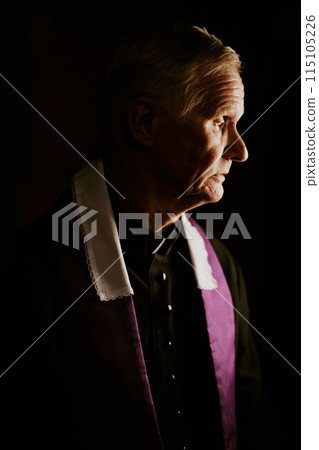 Vertical medium closeup low key of senior Caucasian Catholic pastor wearing soutane and stole working in confessional booth Vertical medium closeup low key of senior Caucasian Catholic pastor wearing soutane and stole working in confessional booth 115105226