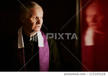 Medium closeup of senior Caucasian Catholic priest talking to penitent in confessional, copy space 115105228