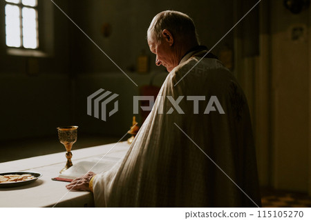Low key shot of senior Caucasian Catholic priest preparing for holy communion rite in church, copy space 115105270