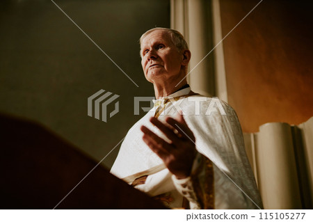 Low angle view medium shot of elderly Caucasian priest preaching sermon in Catholic church, copy space Low angle view medium shot of elderly Caucasian priest preaching sermon in Catholic church, copy space 115105277