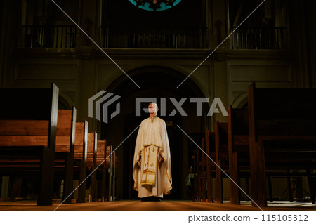 Wide shot of senior Caucasian Catholic priest wearing liturgical vestment standing in empty church, copy space Wide shot of senior Caucasian Catholic priest wearing liturgical vestment standing in empty church, copy space 115105312