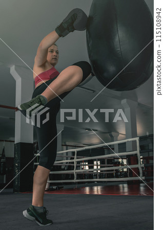 Women's self-defense force. Young female kickboxer is training with a punching bag in the gym. Women's self-defense force. Young female kickboxer is training with a punching bag in the gym. 115108942