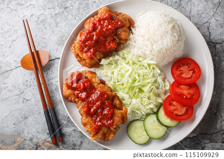Ayam geprek is a typical Indonesian dish of fried chicken with sambal served with white rice, cucumber, tomato and cabbage closeup on the plate. Horizontal top view Ayam geprek is a typical Indonesian dish of fried chicken with sambal served with white rice, cucumber, tomato and cabbage closeup on the plate. Horizontal top view 115109929