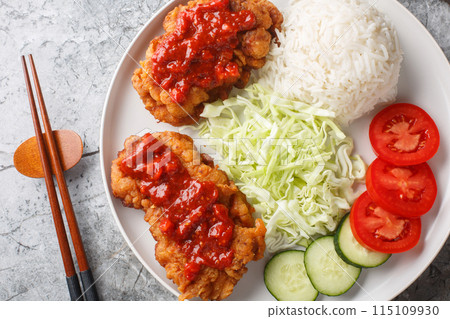 Ayam geprek Crispy Chicken Smashed in Sambal served with white rice, cucumber, tomato and cabbage closeup on the plate. Horizontal top view Ayam geprek Crispy Chicken Smashed in Sambal served with white rice, cucumber, tomato and cabbage closeup on the plate. Horizontal top view 115109930