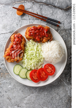 Ayam geprek an Indonesian fried chicken with sambal sauce served with white rice, cucumber, tomato and cabbage closeup on the plate. Vertical top view 115109931