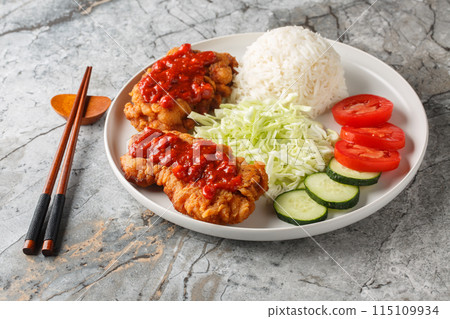 Ayam Geprek Sambal Bawang crispy fried chicken served with white rice, cucumber, tomato and cabbage closeup on the plate. Horizontal Ayam Geprek Sambal Bawang crispy fried chicken served with white rice, cucumber, tomato and cabbage closeup on the plate. Horizontal 115109934