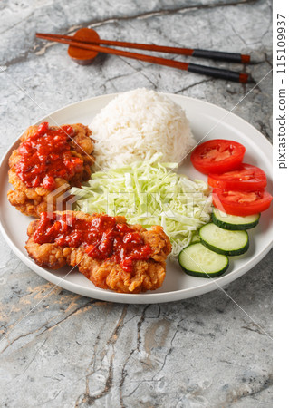 Ayam geprek an Indonesian fried chicken with sambal sauce served with white rice, cucumber, tomato and cabbage closeup on the plate. Vertical 115109937